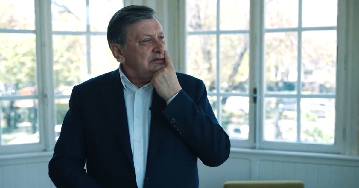 Crin Antonescu, îmbrăcat în costum și cămașă albă, fără cravată, în fața unei ferestre albe, în timp ce își ține degetul pe nas și se gândește