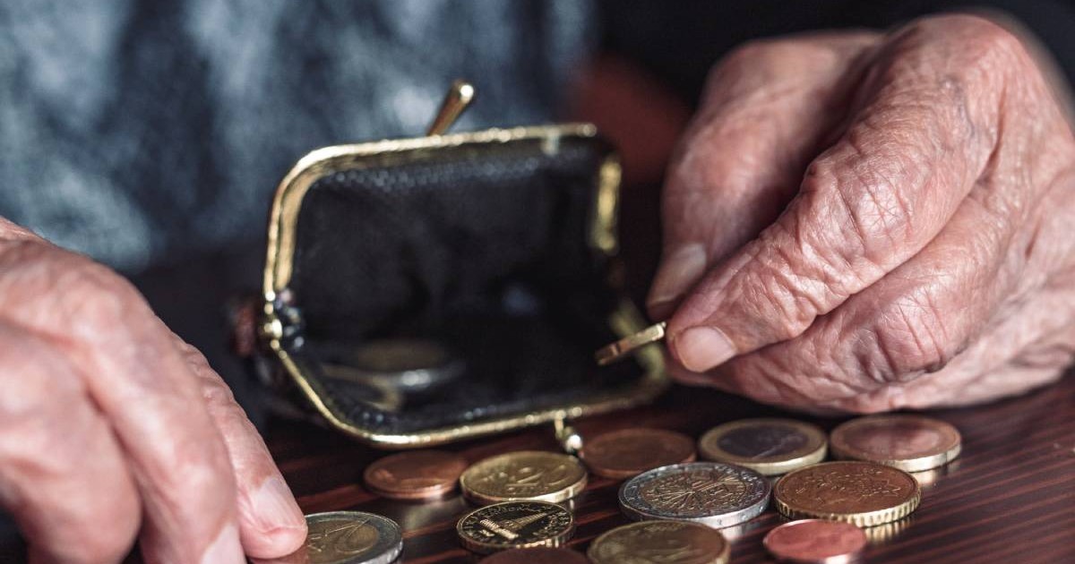 O femeie cu venituri extrem de mici, în timp ce își numără monedele de câte un euro dintr-un portofel. Banii primiți din ajutorul social sunt întinși pe o masă maro