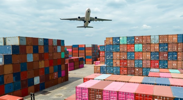 Mai multe containere de transport pentru colete Shein și Temu, sunt așezate într-un port, în timp ce un avion cargo trece pe deasupra lor