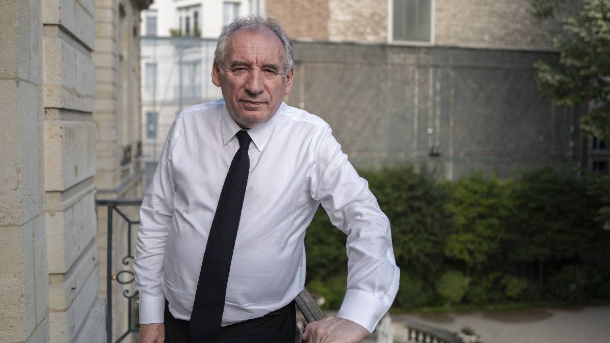 Premierul Franței, Bayrou, îmbrăcat într-o cămasă albă, cu cravată neagră, se sprijină de o balustradă de beton