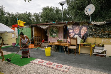 O femeie din tabără dă cu mătura în fața barăcii sale