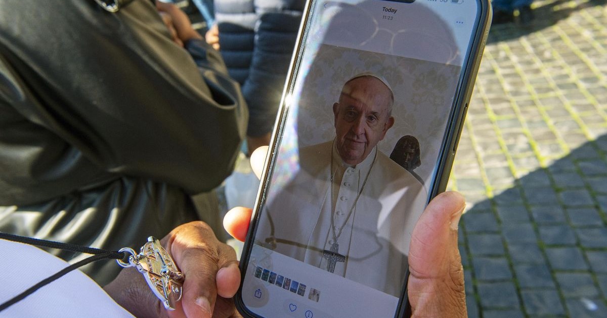 Persoană necunoscută ține în mână un telefon mobil cu o fotografie a Papei Francisc în Piața Sfântul Petru din Vatican