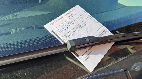 O înștiințare de amendă emisă de poliția locală din Italia, completată de mână pe un formular tipizat, fixată sub ștergătorul de parbriz al unui vehicul.