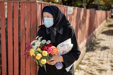 O femeie aşteaptă să participe, de la distanţă, la înmormântarea unei rude
