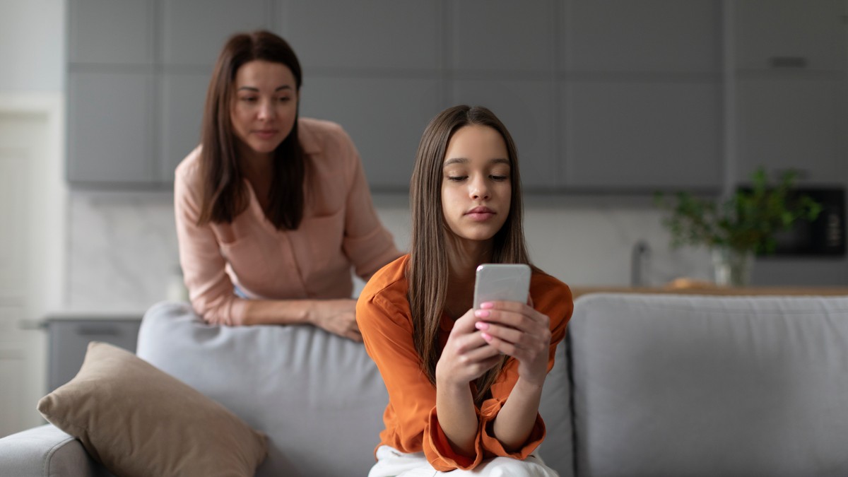 O mama incearca sa se uite la ce scrie fiica sa pe telefon, din spatele ei.