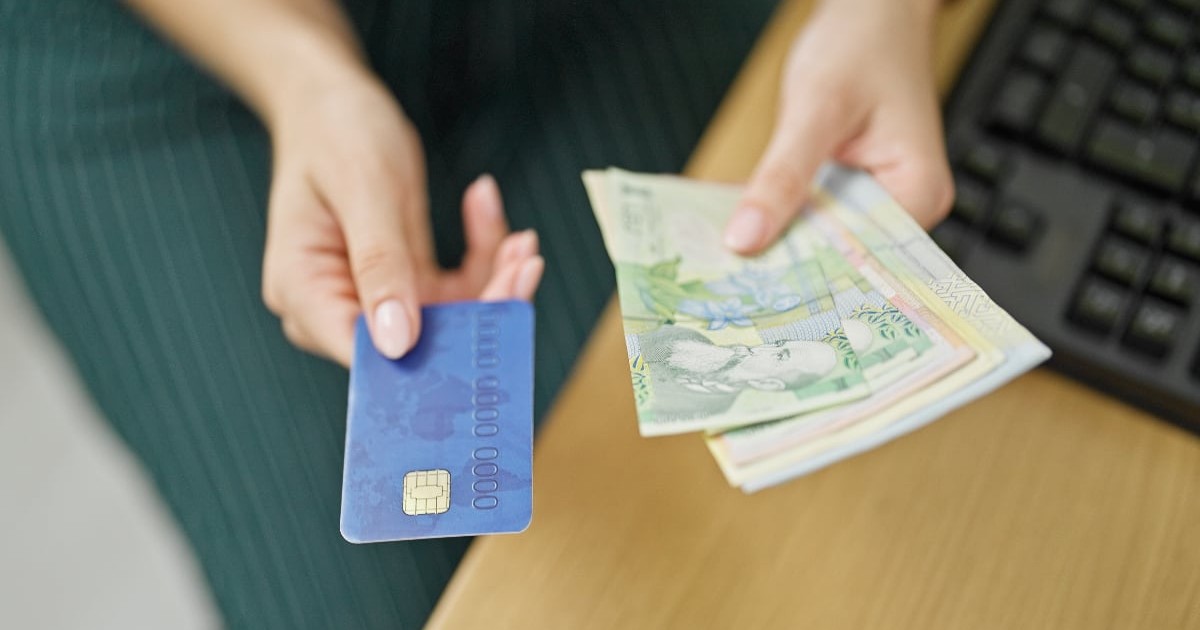 O femeie care ține în mână un card de credit și mai multe bancnote de un lei, 10 lei și 50 de lei