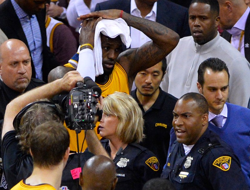epa04794505 Cleveland Cavaliers forward LeBron James (C) covers his head with a towel after falling on a television cameraman on the baseline after getting fouled as Cleveland Police surround him in the first half of Game Four of the NBA Finals at Quicken Loans Arena in Cleveland, Ohio, USA, 11 June 2015. EPA/LARRY W. SMITH CORBIS OUT
