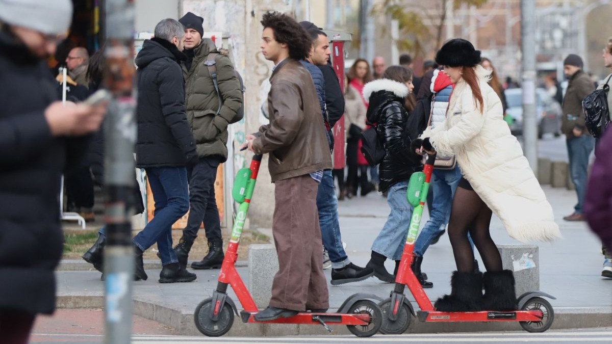Doi oameni merg pe trotinete electrice, iar alții pe stradă, îmbrăcați cu geci, într-o zi rece de primăvară, zona Piața Romană, București, 3 martie 2025