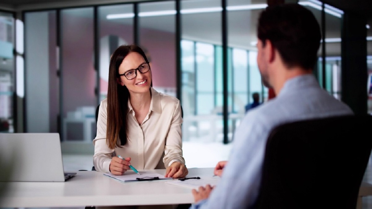 Un barbat, imbracat cu o camasa albastra, se afla la un interviu de job, cu o femeie de la HR, imbracata office cu o camasa alba