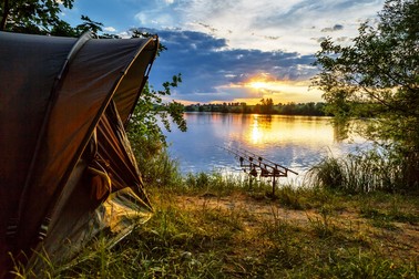 Fishing adventures, carp fishing. Angler, at sunset, is fishing with carpfishing technique. Camping on the shore of the lake.Carp Fishing Sunset