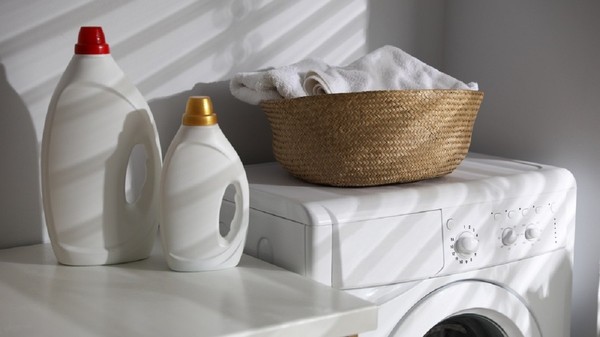 Coş de rufe pe o maşină de spălat, alături de recipiente detergent pe un blat de bucătărie