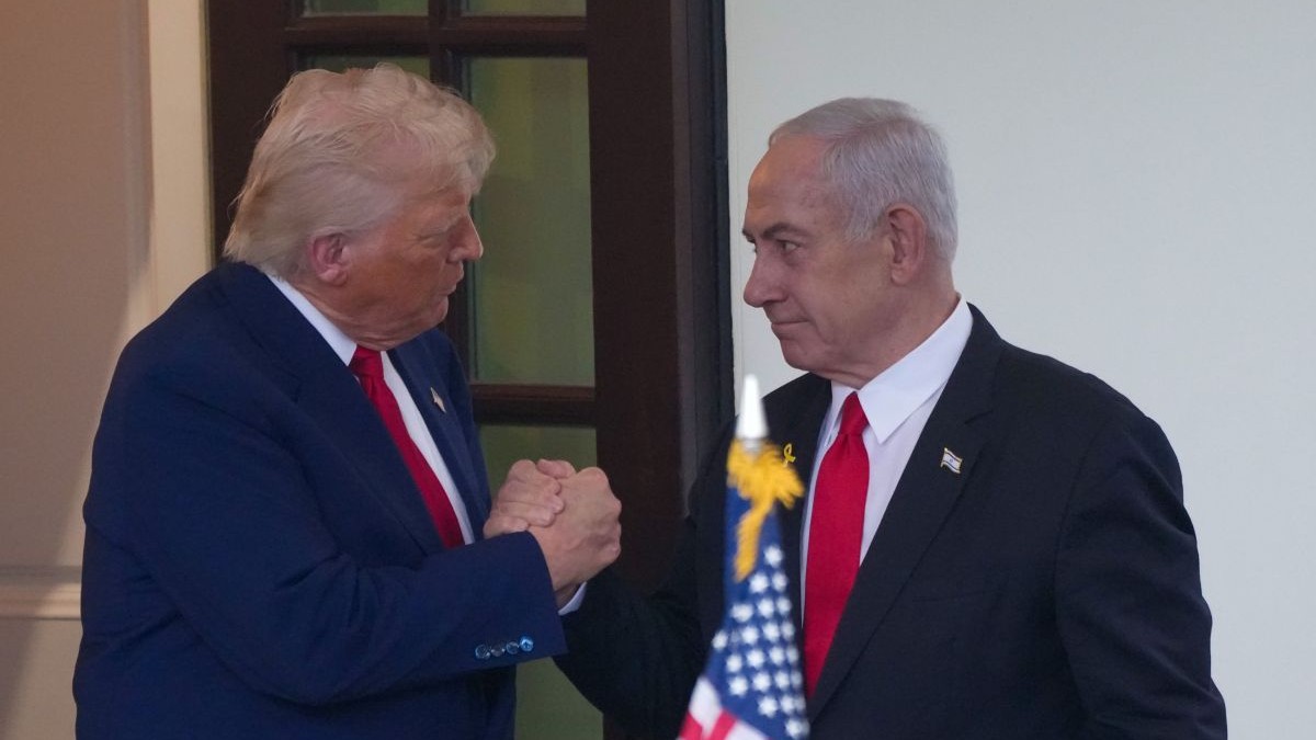 Donald Trump dă mâna cu Benjamin Netanyahu stând în picioare și având în față un steag american, aprilie 2025