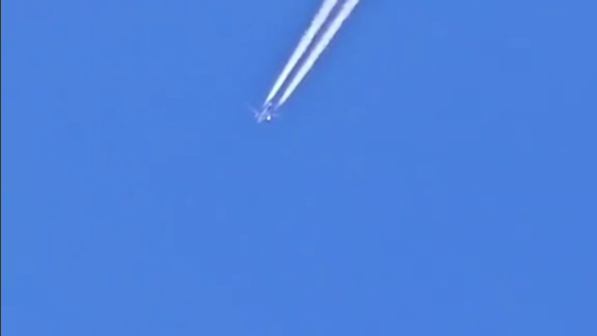 un avion zburând pe cer, care lasă în urmă o dâră. Sub el, un obiect în formă de disc
