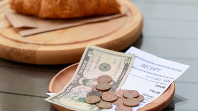 Țări în care bacșișul nu este permis - Pe o masa se afla un croissant, așezat pe un platou de lemn, iar lângă el  un alt vas rotund de lemn pe care se afla nota de plata si banii