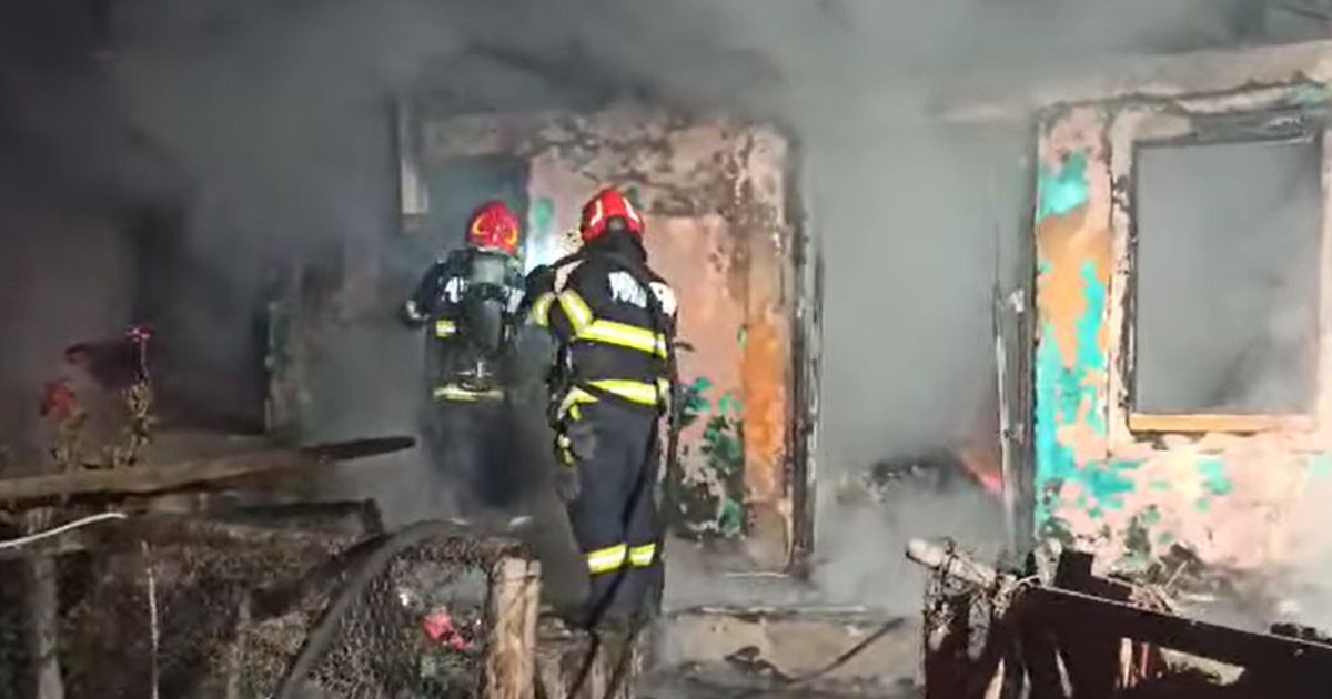 doi pompieri echipați complet, cu căști roșii, uniforme negre cu dungi reflectorizante galbene și aparate de respirat pe spate încercând să stingă focul izbucnit la o casă din Vaslui, localitatea Orgoieşti, noaptea de 26 spre 27 iunie 2025