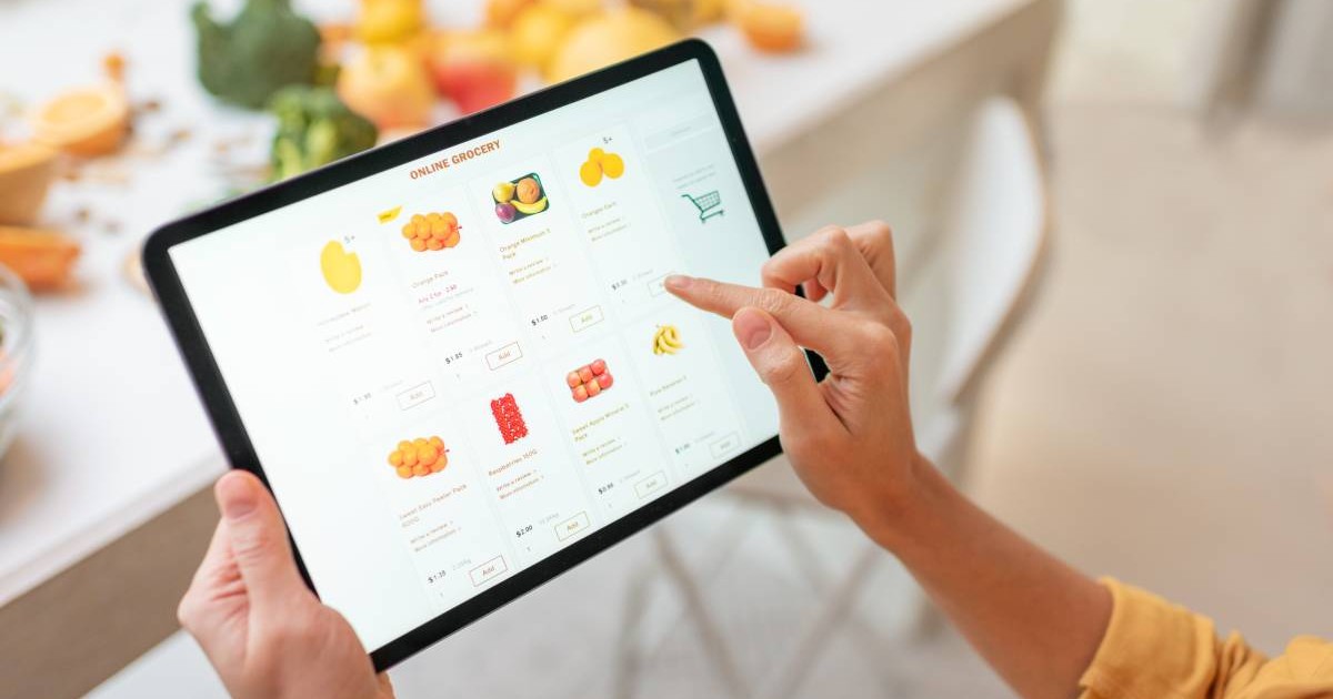 O femeie cu o tabletă în mână, în timp ce face cumpărături online și comandă fructe dintr-o aplicație.