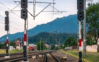 Trei linii de cale ferată într-o gară dintr-o zonă montană din România, luminile roșii de semnalizare sunt aprinse