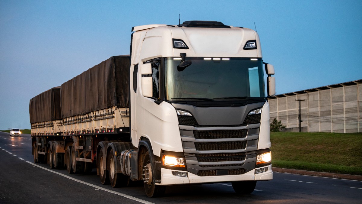 Un camion cu cabină albă care circulă pe șosea
