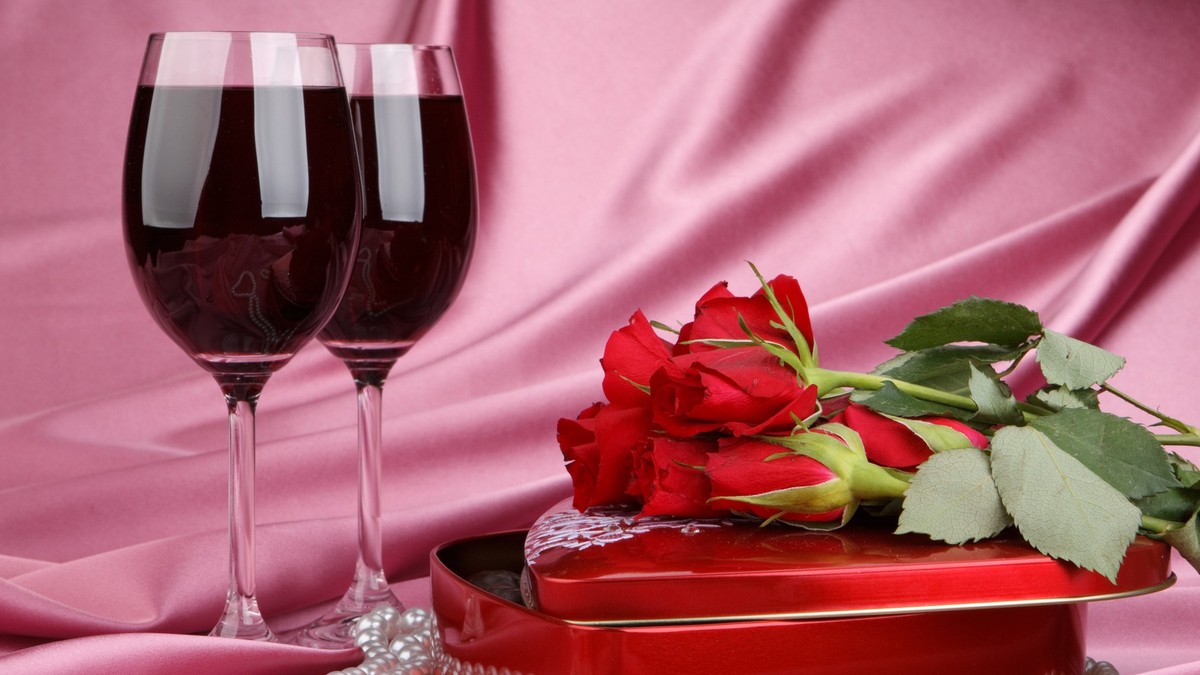 Imagine cu o cutie roșie în formă de inimă, două pahare de vin roșu și un buchet de trandafiri roșii