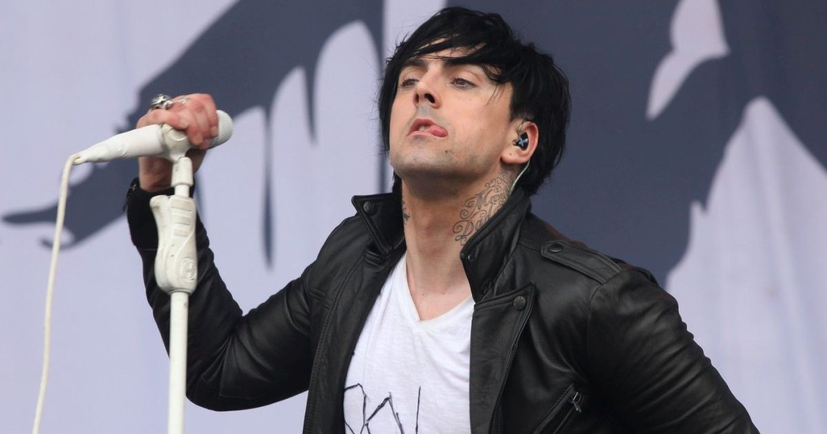 Solistul trupei Lostprophets, Ian Watkins, îmbrăcat cu un tricou alb și geacă de piele, este pe scenă la concertul V Festival Weston Park 2011 și scoate limba