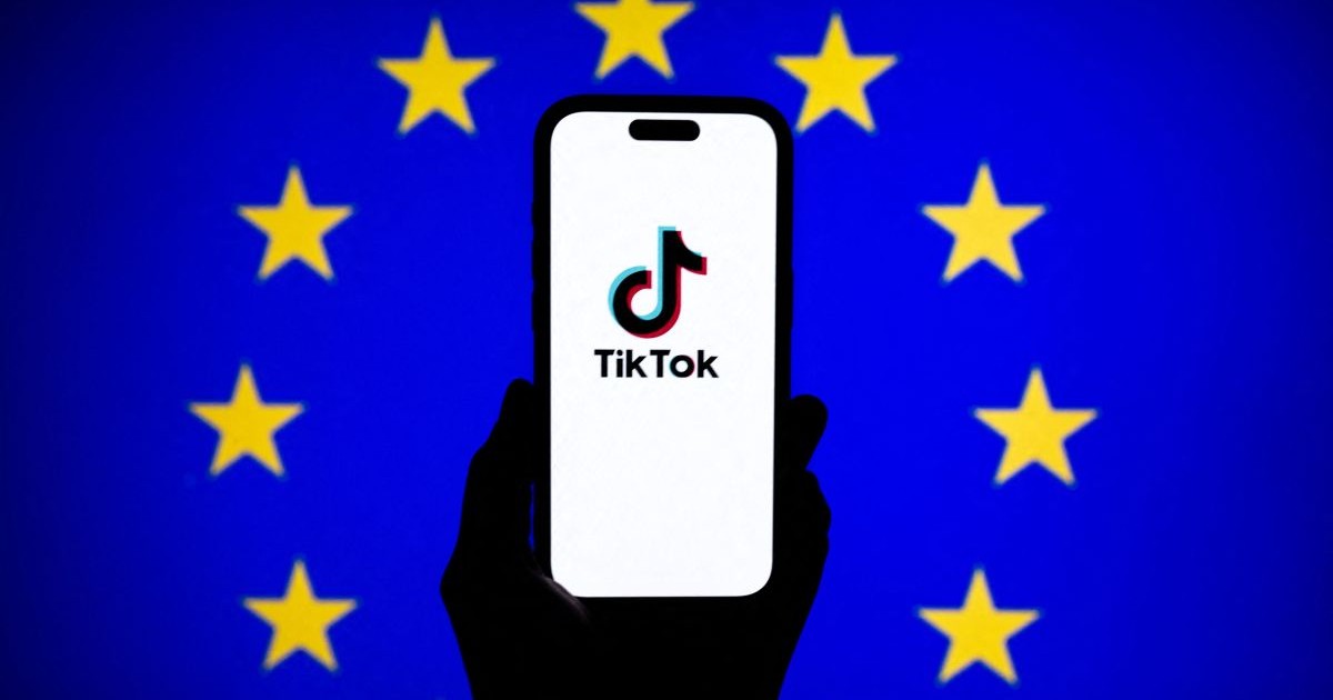 Logo-ul TikTok este afișat pe ecranul unui telefon mobil în fața unui ecran de computer care afișează steagul UE, ianuarie 2026