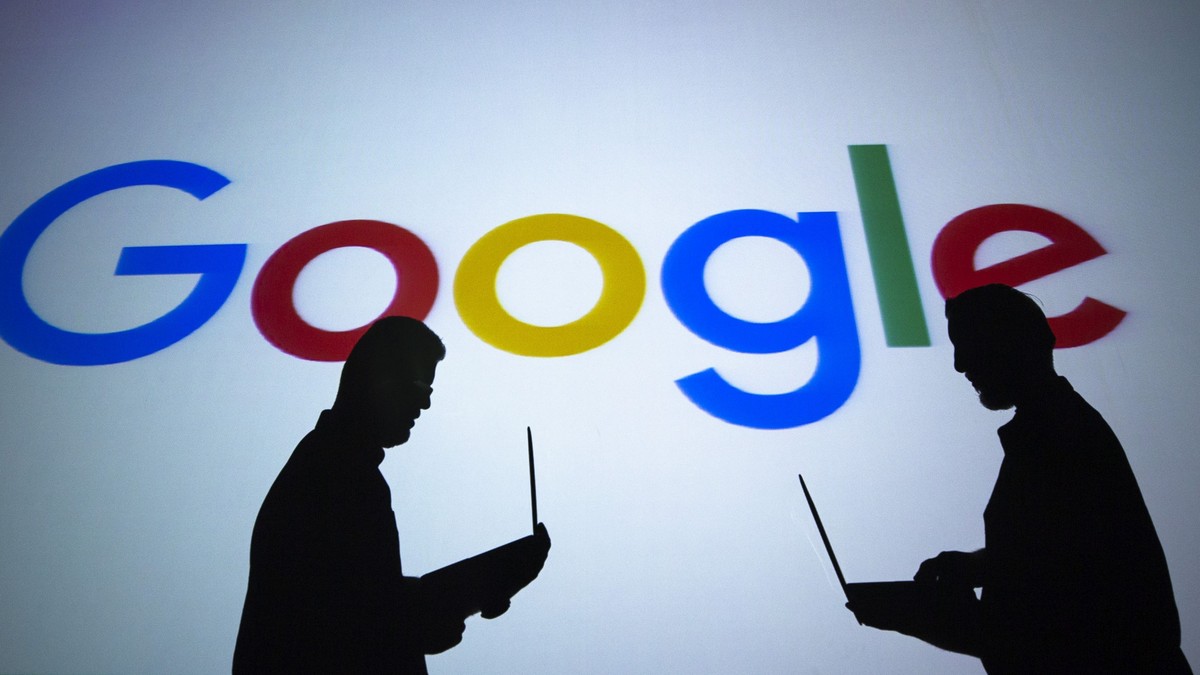 Google a depășit o mie de miliarde de dolari ca valoare. Sigla Google cu siluetele a doi oameni stând la laptop