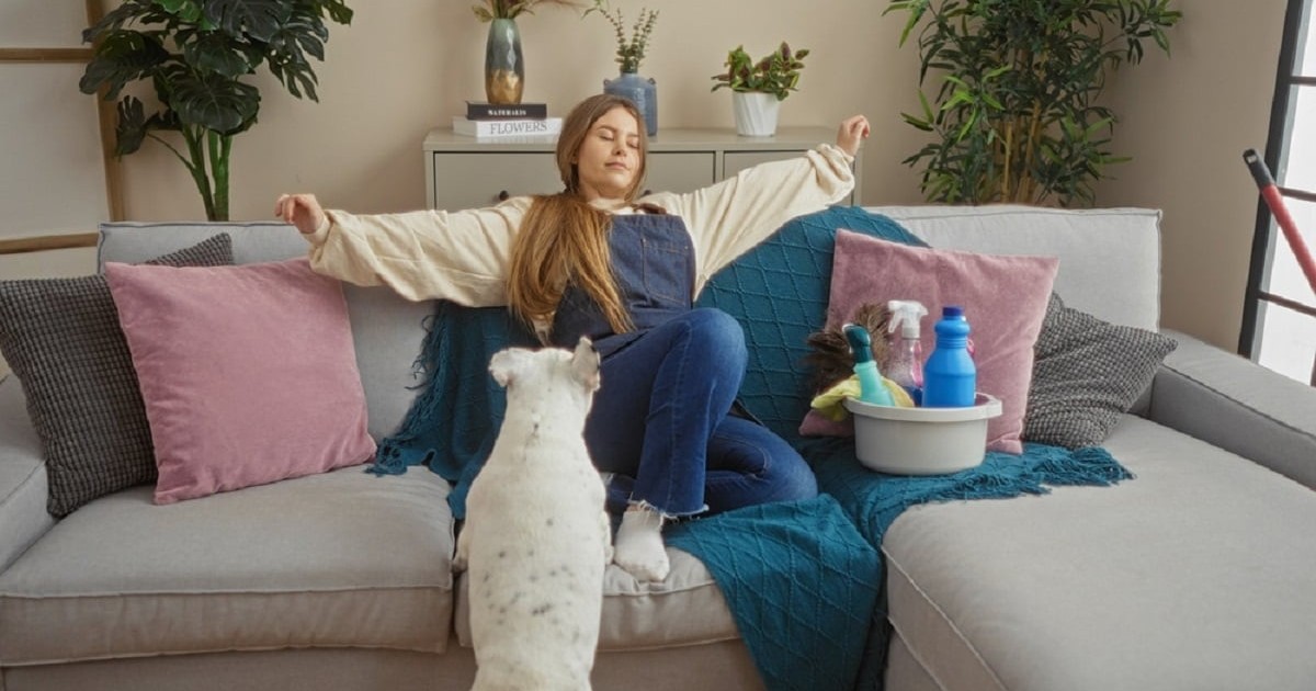 Trucuri pentru o casă mereu curată când ai animale de companie - O tânără se relaxează pe canapea după ce a terminat curățenia, iar catelul ei se uita la ea