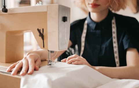 O croitoreasă cu un centimetru de croitorie în jurul gâtului, ghidând atent un material textil alb la o mașină de cusut electrică.