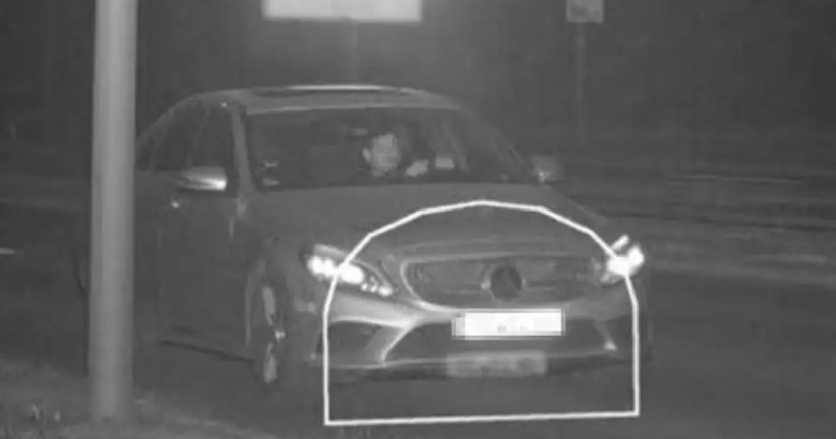 Imaginea alb-negru, capturată de o cameră de supraveghere pe timp de noapte, surprinde un Mercedes-Benz în trafic, având partea frontală și numărul de înmatriculare evidențiate de un chenar grafic.