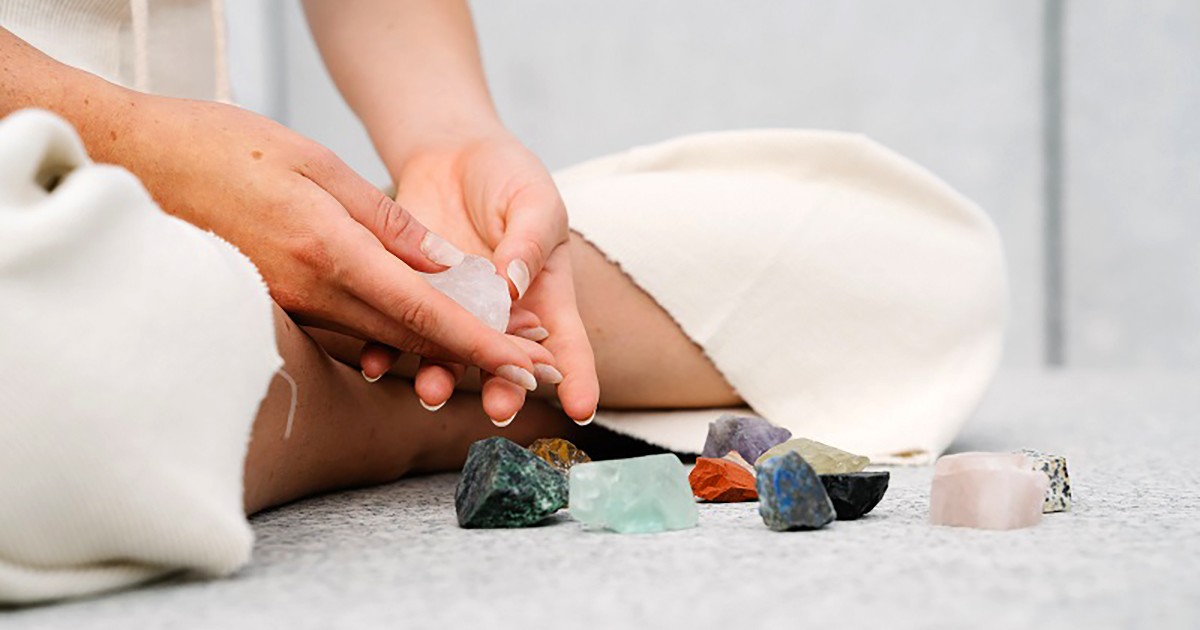 Femeie care sta turceste pe podea, are in fata ei diferite cristale pentru meditatie