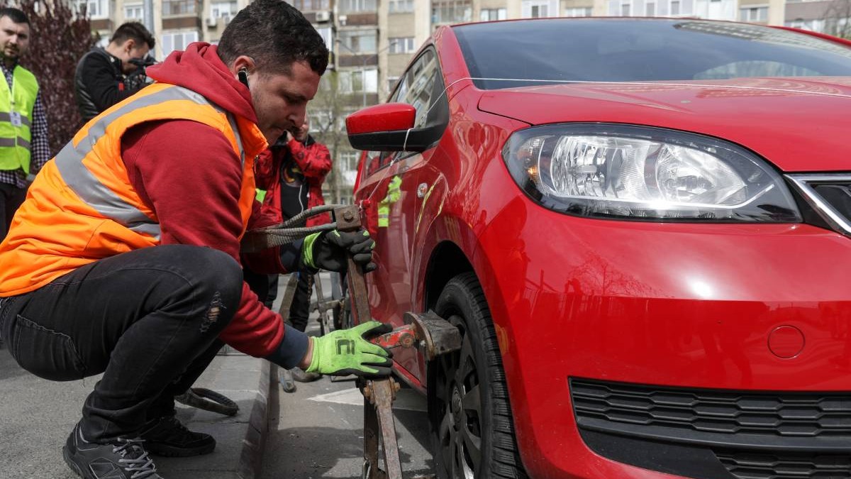 barbat care pune blocator roata unei masini rosii care este oprita intr-o zona interzisa