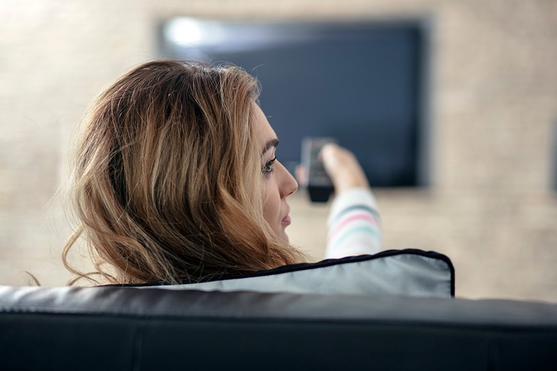 Beautiful woman lying on a sofa with remote control and watching television.