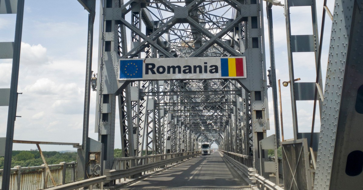 Podul Giurgiu-Ruse, podul Prieteniei, văzut dinspre Giurgiu. Pe șosea se află un TIR alb, iar deasupra ramei metalice ale podului se observă un semn de circulație cu textul „România”, steagul Uniunii Europene și steagul României