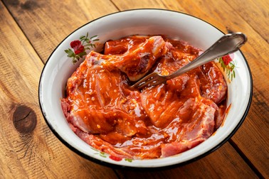 raw meat marinated in sauce for barbecue in a metal Cup on a wooden table