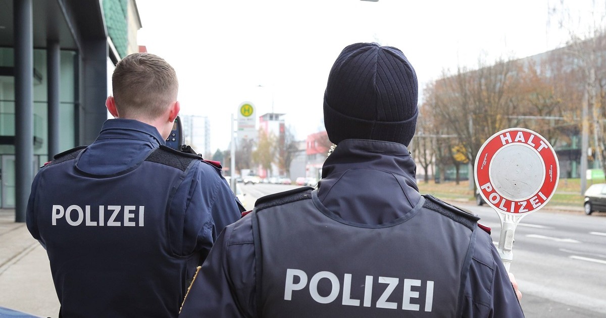 Doi polițiști cu spatele, unul ține în mâna dreaptă o paletă cu semnul stop, celălalt un aparat de măsurare a vitezei mașinilor.