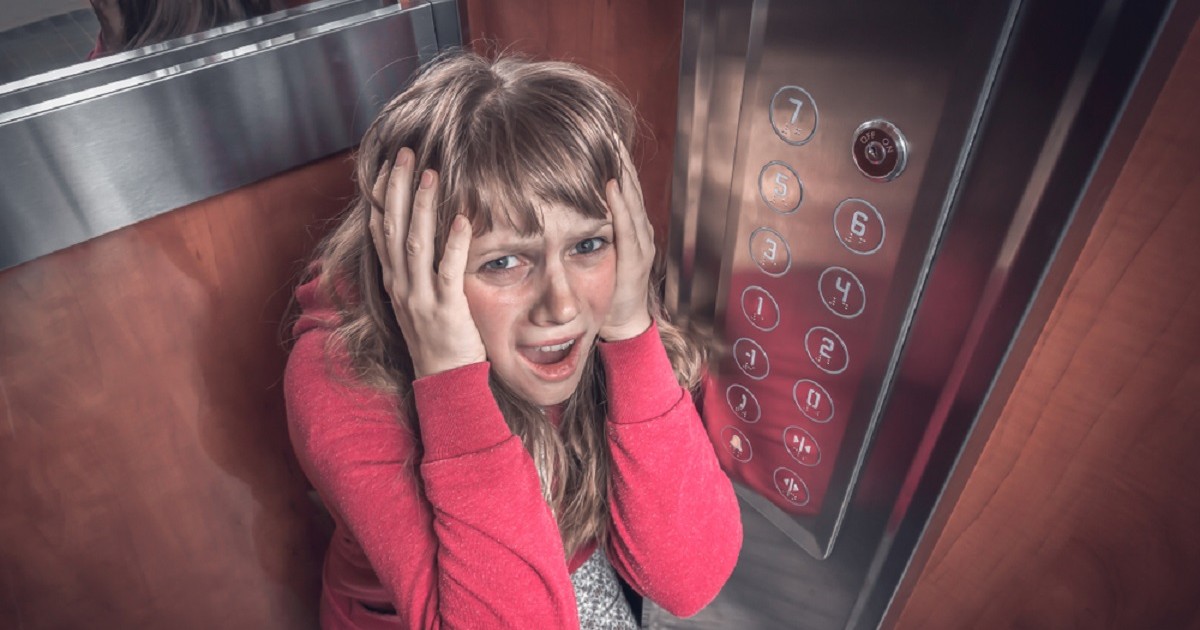 Ce înseamnă când visezi lift - O femeie, cu o bluză roșie, își ține mîinile pe cap, părând îngrozită de faptul că este blocată într-un lift