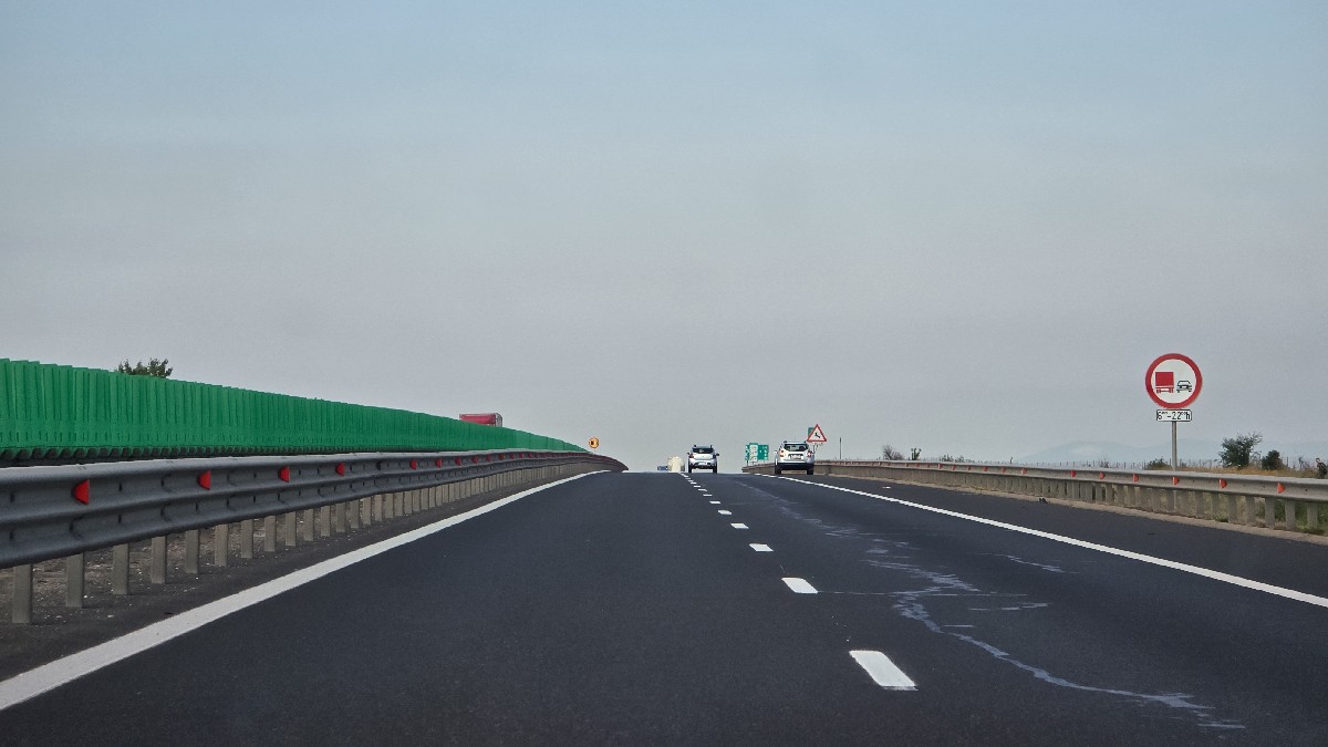 O secțiune a autostrăzii A1 din România, cu un drum cu mai multe benzi, separat de balustrade metalice și panouri verzi înalte pentru protecție antiorbire