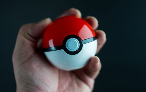 O mână ține o minge Pokémon pe un fundal negru