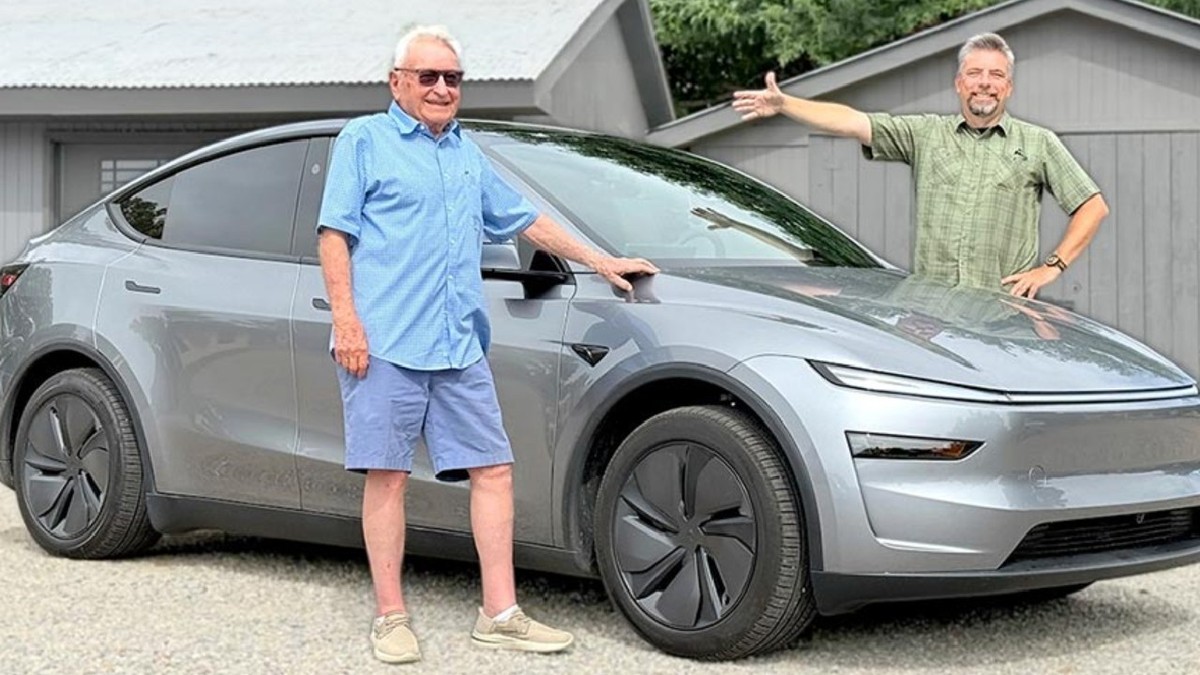 Un bărbat de 98 de ani, cu camasa albastra si pantaloni scurti albastri, langa o masina Tesla gri, pe partea opusa, un bărbat cu camasa verde