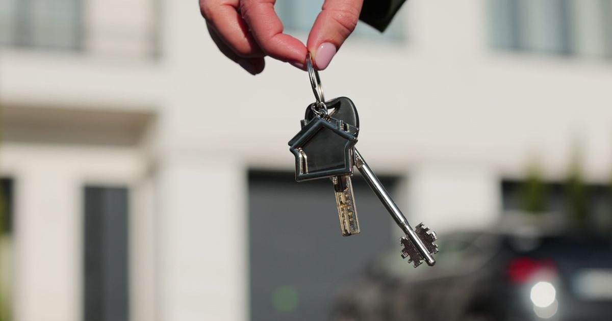 Prim-plan cu două chei și un breloc cu o casă, în mâna unei femei pe fundal. Concept imobiliar pentru cumpărarea unei case noi.
