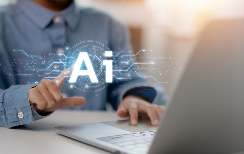 Un bărbat la laptop foloseste inteligenta artificiala la laptop, poartă o cămașă albastră și stă la un birou alb. În stânga imagini este și o grafică au AI