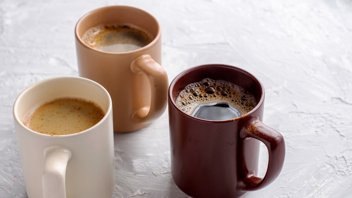 În imagine sunt trei cești de cafea așezate pe o suprafață albă, fiecare având o nuanță diferită. Cafeaua din cești este proaspăt preparată și prezintă un strat fin de spumă la suprafață.
