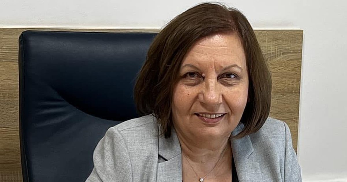 Șefa ANM, Elena Mateescu, îmbrăcată cu o bluză neagră și un sacou gri, stă pe un scaun negru cu spătar înalt, la un birou