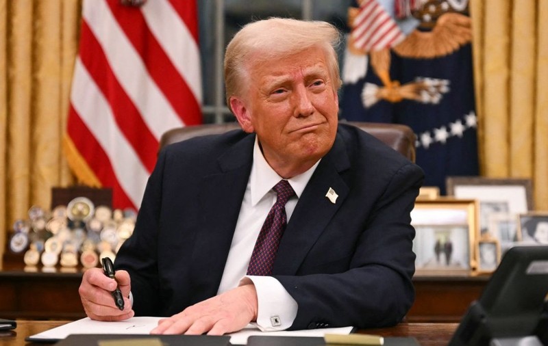 Donald Trump, îmbrăcat în costum, în timp ce stă la Biroul Oval, la Casa Albă, și semnează un document, în ianuarie 2025