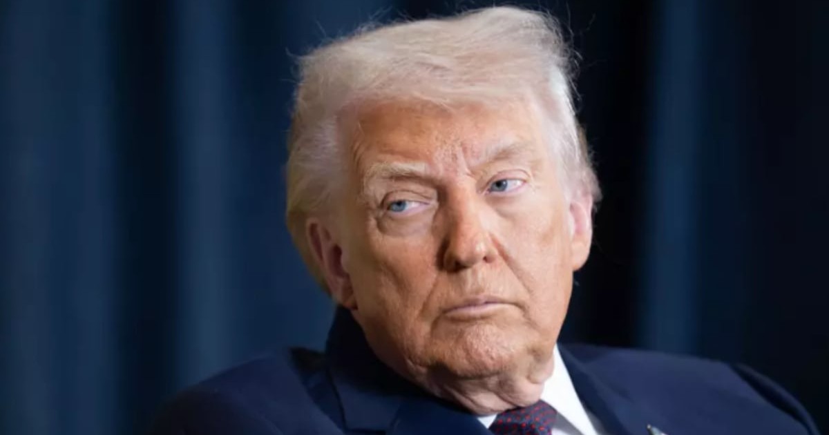 Donald Trump într-un sacou albastru închis în timp ce stă jos și privește în lateral.