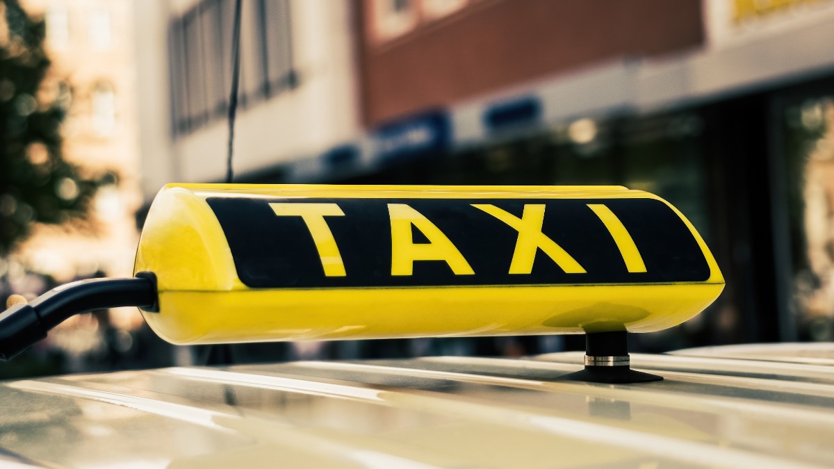 Un semn galben pe care scrie TAXI, montat pe plafonul unui vehicul.