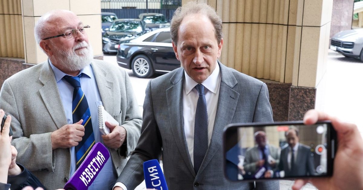 Ambasadorul Germaniei la Moscova, Alexander Graf Lambsdorff, in costum gri, cămașă albă și o cravata neagra, la Ministerul Afacerilor Externe al Rusiei, inconjurat de reporteri, microfoane si telefoane, in stanga fotografiei, langa ambasador, un jirnalist supraponderal, grizonat și cu barbă, care tine la piept un carnetel