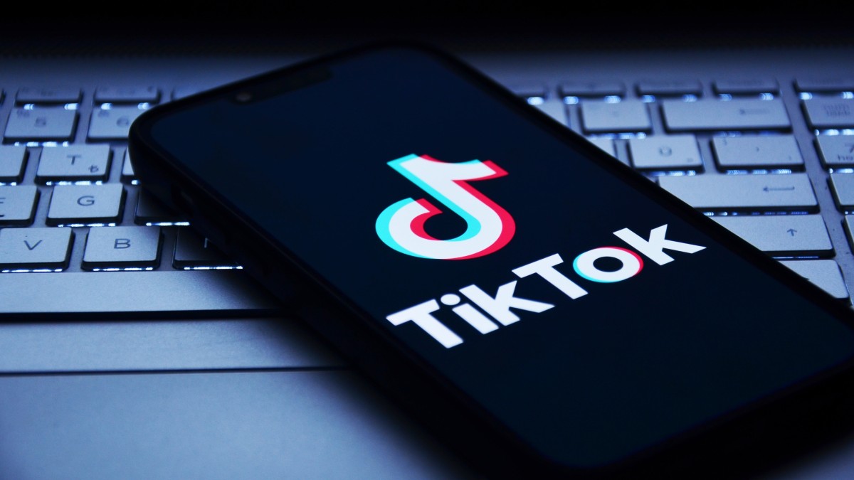 Telefon mobil pe care este deschisă aplicația TikTok. Este așezat pe tastatura unui laptop