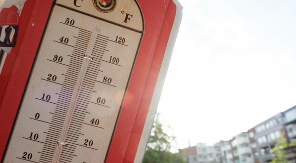 Un termometru de exterior în stil vintage, cu margine roșie, indicând o temperatură  de aproape 35°C în lumina soarelui.