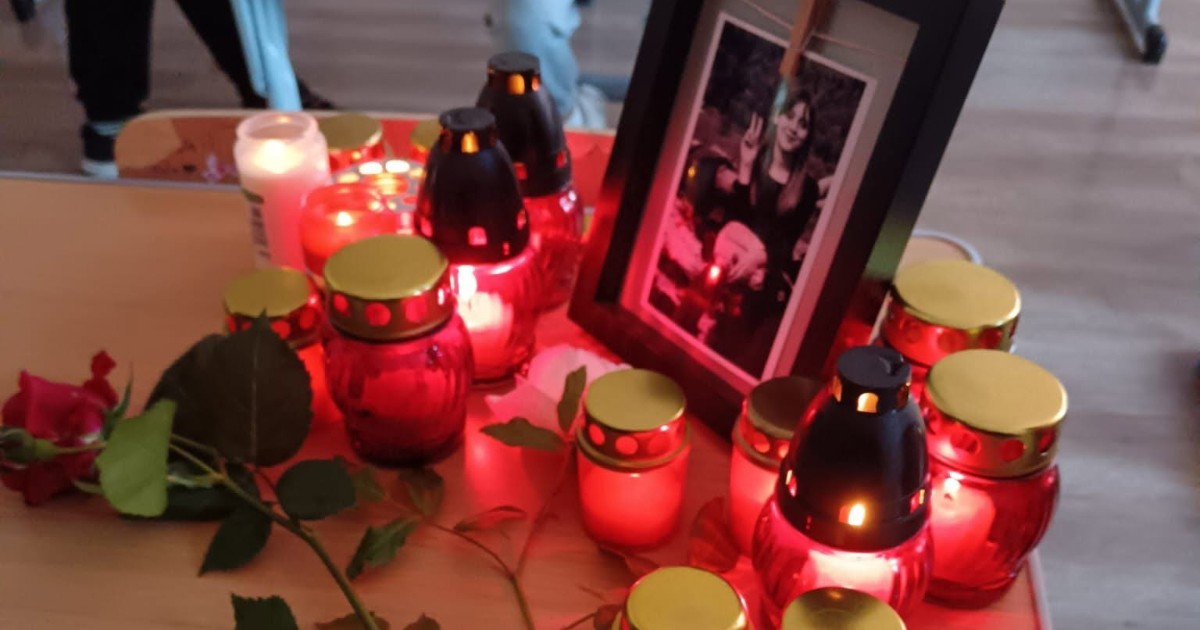 Un mic altar comemorativ amenajat pe o bancă, compus dintr-o fotografie înrămată a unei tinere fete, un trandafir roșu și numeroase candele aprinse.